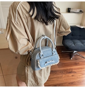 Detailed view of blue denim handbag with white lace bow and gray leather piping detail