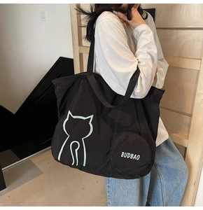 Detail of a large black tote bag featuring a green cat outline and a small round pouch