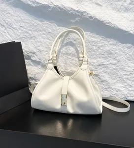 Detail of a white patent leather handbag with gold buckle, strap, and lifestyle background
