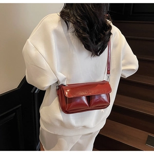 Detail of dark red glossy leather shoulder bag with two front pockets and silver hardware
