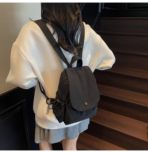 Rear view of a model wearing a compact black nylon backpack with a flap and drawstring