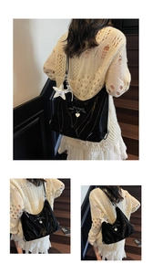 Detail of black glossy hobo bag with bow decoration and silver heart pendant charm