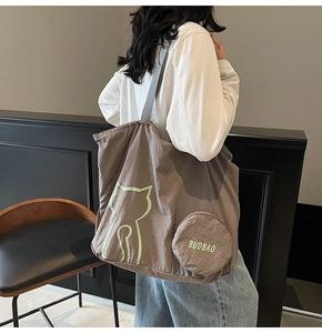 Detail of tan tote bag featuring green cat pattern and matching round charm on a model