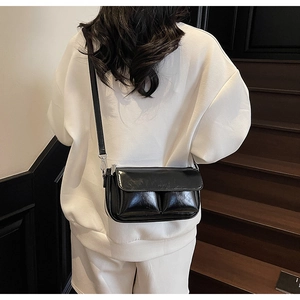 Detail view of a black glossy baguette bag with front pockets on a shoulder strap