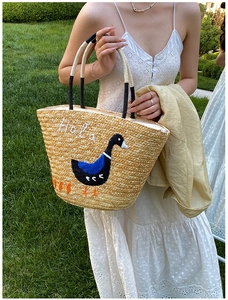 Detail of hand-woven straw tote with embroidered Hala text and goose pattern