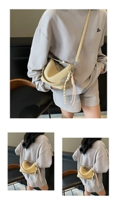Detail of a beige moon-shaped leather shoulder bag with a black and white braided charm