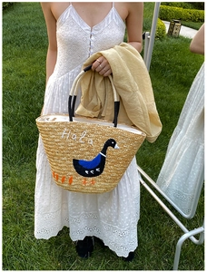 Detail view of woven straw tote bag with duck embroidery and black wrapped handle