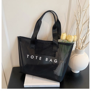 Détail du sac cabas en maille noire avec texte TOTE BAG blanc sur un socle épuré