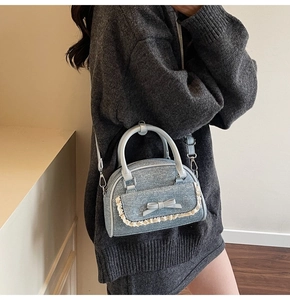 Close-up of light blue denim bow handbag with cream lace trim on a grey sweater