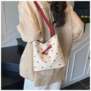 Detail of white leather bucket bag featuring red bow prints and heart charm accessory