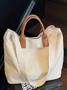 Minimalist canvas tote bag with brown leather handles and green letter print detail