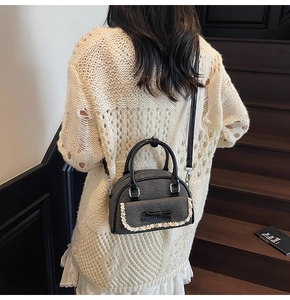Detail of grey crossbody bag with lace bow decoration and silver metal hardware accents