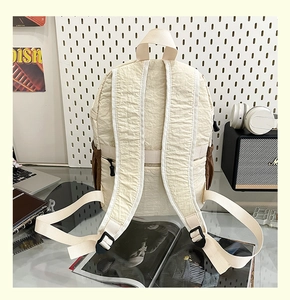 Vista posteriore dettagliata di uno zaino in nylon crema con tasche laterali marroni e cinghie