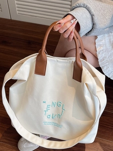 Minimalist beige canvas tote bag with brown leather handles and blue embroidery