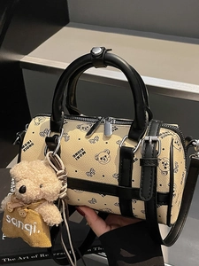 Chic beige cylinder Boston bag with bear patterns, top handles, and plush charm