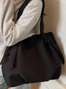 Minimalist black tote bag with decorative knot details and wide shoulder straps