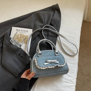Detailed close-up of blue denim bow handbag with lace trim on a grey suit background