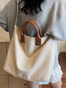Large beige canvas tote bag with brown leather handles and adjustable shoulder strap