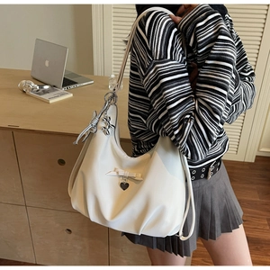 White pleated hobo bag with bow detail and silver heart pendant on a model