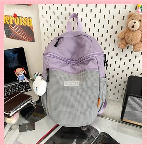 Dettaglio di uno zaino bicolore viola e grigio con un ciondolo a forma di palla di pelo