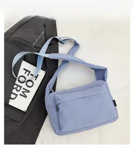 Detail showing light blue nylon crossbody bag with large front zipper pocket and wide strap