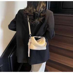 Detail view of cream lychee leather hobo bag with pink woven pendant on a model