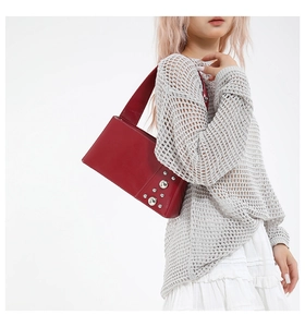 Red leather shoulder bag with silver rivet details shown on model in minimal studio setting