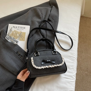 Detail of grey twill Boston bag featuring white lace trim and black leather bow accent