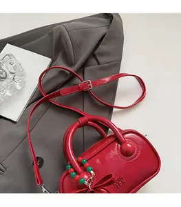 Macro detail of red patent leather pillow bag with large bow and decorative bead charm