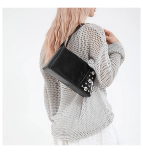 Model wearing black punk style shoulder bag with silver rivet details and glossy finish