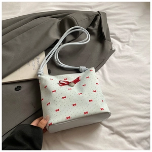 Detail of light blue crossbody bag with red bow prints and heart pendant decoration