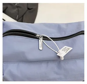 Detail view of high-quality smooth metal zipper and logo tag on nylon crossbody bag