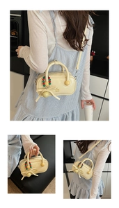 Chic cream-colored mini boston bag with bow detail and beaded charm shown in a room