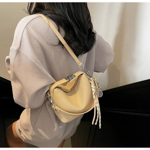 Detail of light yellow lychee grain leather bag with silver metal buckle and braided charm