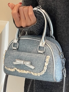 Blue denim handbag with silver bow detail and lace trim shown held by a model