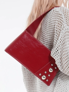 Glossy red shoulder bag with silver rivet studs worn with a beige crochet knit sweater