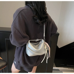 Detail of silver pebble grain crossbody bag featuring woven cord and pink ribbon charms