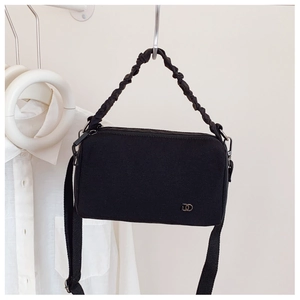 Détail du sac Boston noir avec poignées tressées et logo argenté sur fond minimaliste