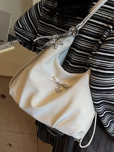 Chic beige hobo bag with leather bow and heart pendant shown on model's shoulder