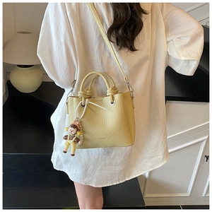 Detail of light yellow leather bucket bag featuring round handles and cute doll pendant