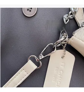Detail of silver chain and IT CHICK EST 1985 leather tag on cream baguette bag