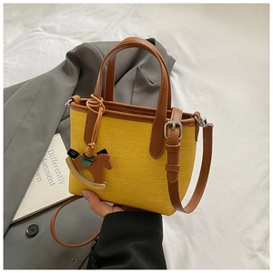 Detail of yellow woven tote bag featuring brown leather straps and wooden horse charm