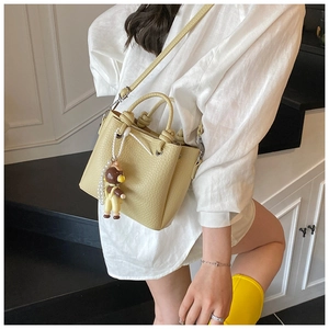 Detalle de bolso tote beige claro con textura de lichi y colgante de oso con perlas