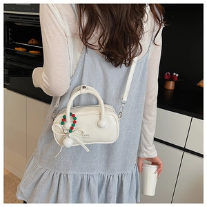 Chic beige pillow bag with ball ornament and bow charm detail shown on model