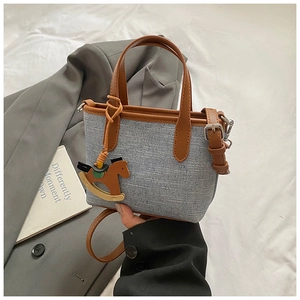 Detail view of canvas tote with brown leather trim and horse charm on a grey suit background