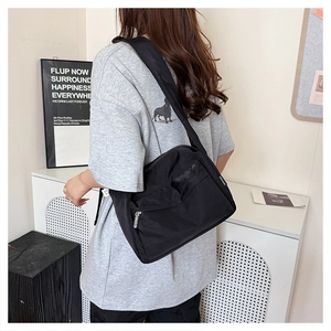 Detail of a black nylon crossbody bag with dual zipper pockets and adjustable wide strap