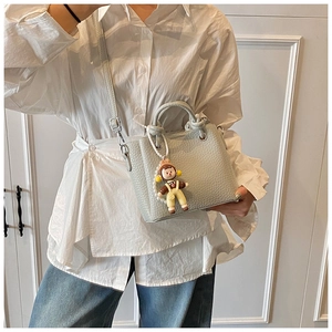 Close-up of mint green pebble leather mini bucket bag with cartoon doll pendant accessory