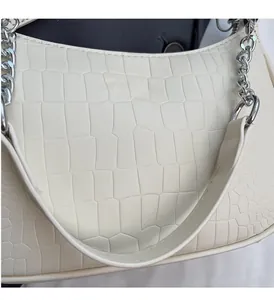 Detailed macro of white faux crocodile texture and silver chain links on a baguette bag