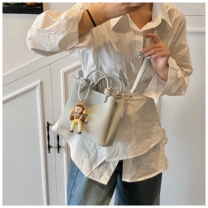 Detail of light gray mini tote bag with litchi grain texture and cartoon girl pendant