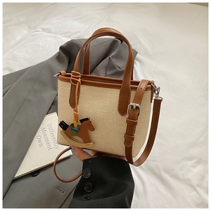 Close-up of beige woven canvas handbag featuring brown leather trim and a wooden horse charm